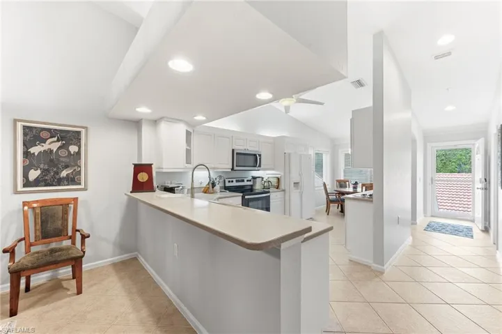 Kitchen with stainless steel appliances, a peninsula, light countertops, white cabinets, and vaulted ceiling