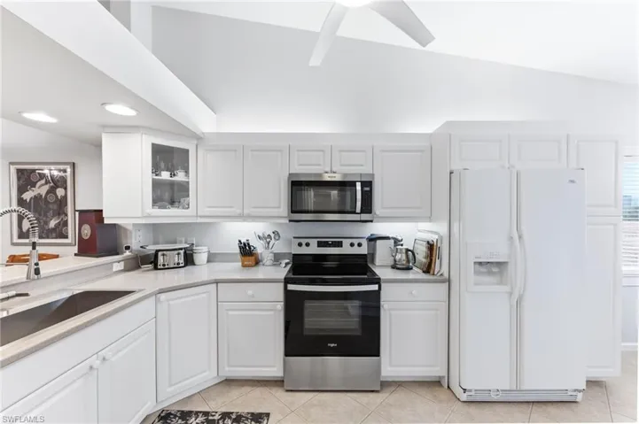 Kitchen with stainless steel appliances, lofted ceiling, white cabinets, glass fronted cabinets, and a ceiling fan