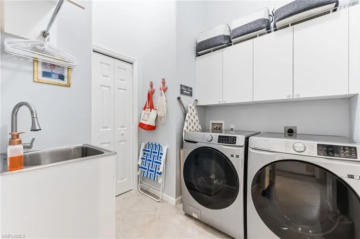 Laundry area featuring washing machine and dryer, cabinet space, and light tile patterned floors