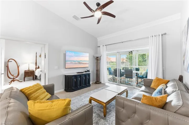 Living area featuring vaulted ceiling, a ceiling fan, light tile patterned floors, and ornamental molding