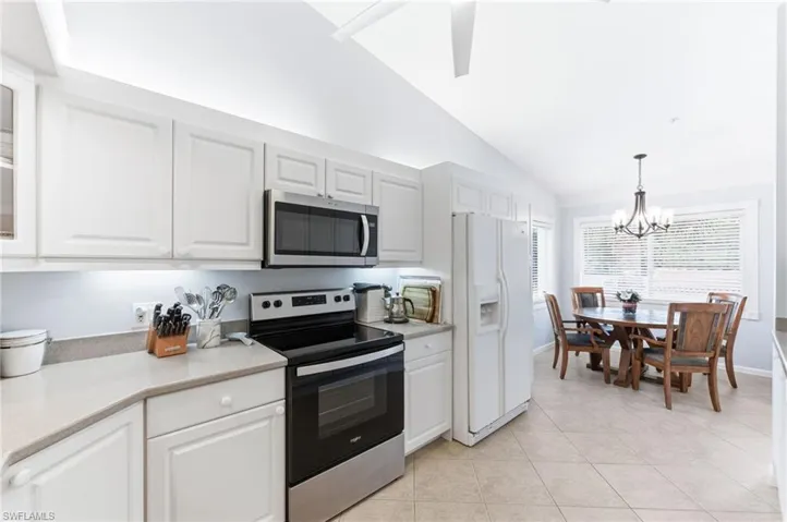 Kitchen with stainless steel appliances, vaulted ceiling, white cabinetry, hanging lights, and light tile patterned flooring