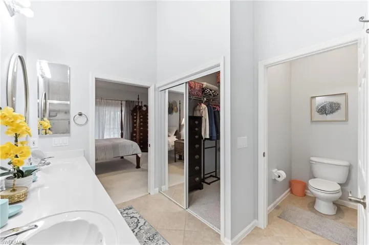 Ensuite bathroom with double vanity, a high ceiling, light tile patterned flooring, and a walk in closet