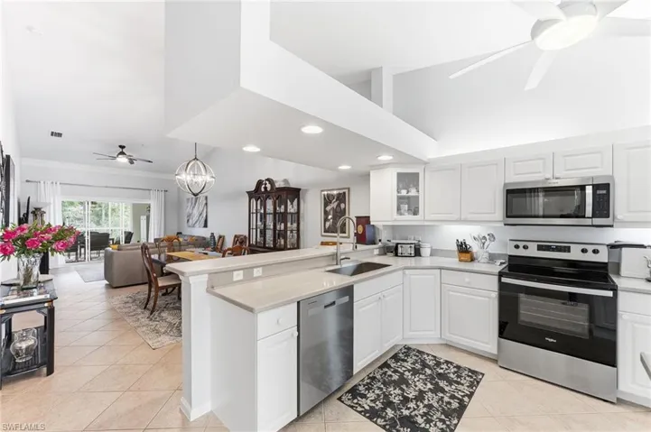 Kitchen with ceiling fan, stainless steel appliances, a peninsula, white cabinetry, and vaulted ceiling