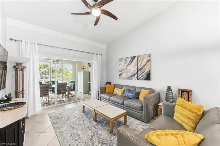 Living area featuring vaulted ceiling, a ceiling fan, light tile patterned flooring, and ornamental molding