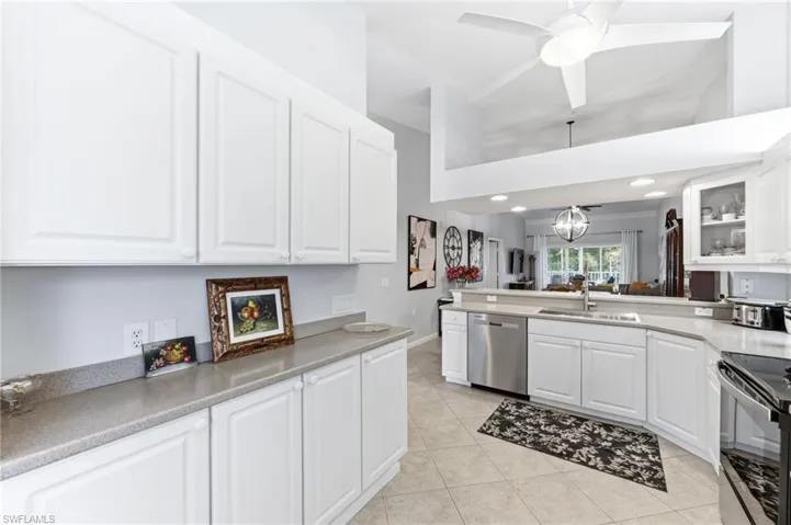 Kitchen featuring white cabinets, stainless steel dishwasher, a ceiling fan, a peninsula, and a high ceiling