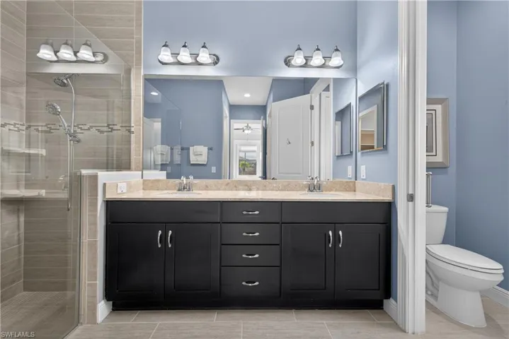 Primary bathroom featuring a tiled shower, double vanity and private water closet.