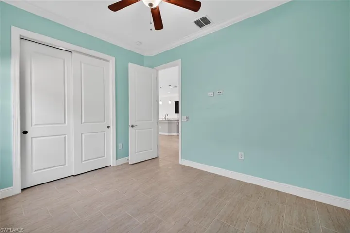 Guest bedroom with tile floors, crown molding and ceiling fan.