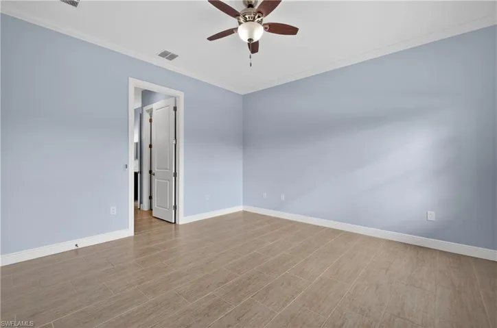 Primary bedroom with crown molding, tiled floors, and ceiling fan.