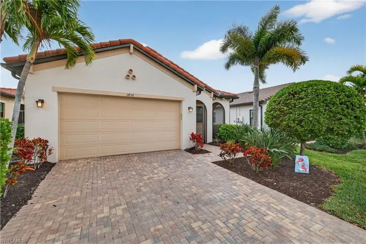 Front of home with a paver driveway, 2 car attached garage, screened front porch and landscaping