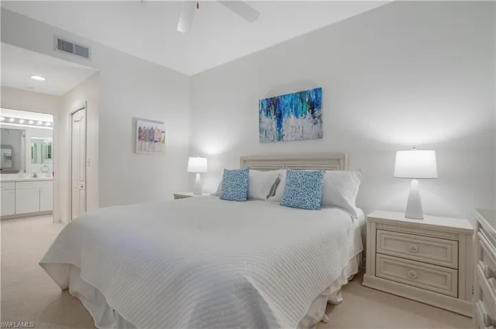 Bedroom with ceiling fan, light colored carpet, and ensuite bath