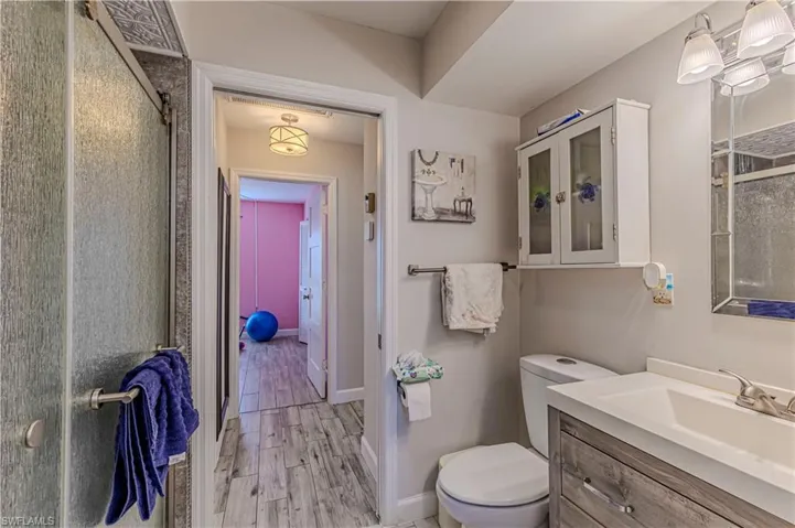 Bathroom with an enclosed shower, toilet, wood finished floors, baseboards, and vanity
