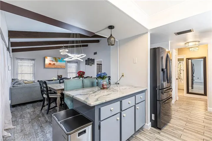 Kitchen featuring light wood-type flooring, a notable chandelier, open floor plan, stainless steel fridge with ice dispenser, and vaulted ceiling with beams
