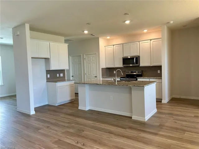 Kitchen with appliances with stainless steel finishes, backsplash, light wood-style floors, a kitchen island with sink, and dark stone counters
