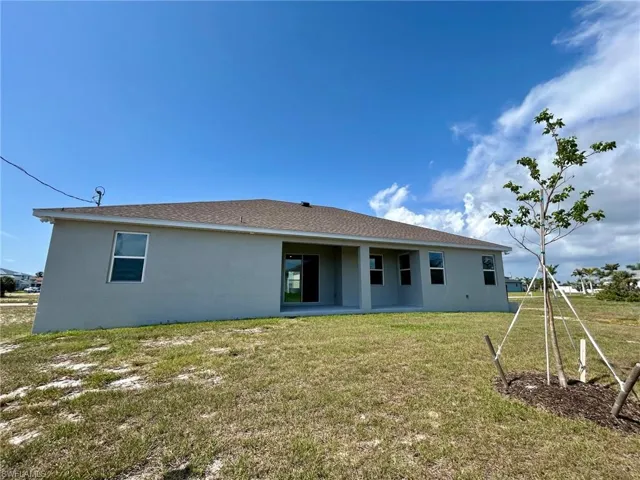 Rear view of property with stucco siding, a yard, and a shingled roof