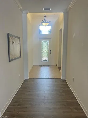 Foyer with glass entry door, crown molding, and tile and wood-style flooring