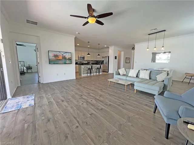 Living room with crown molding, wood-type flooring, and ceiling fan