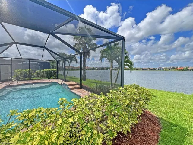 View of swimming pool with enclosure, lawn, and lake view