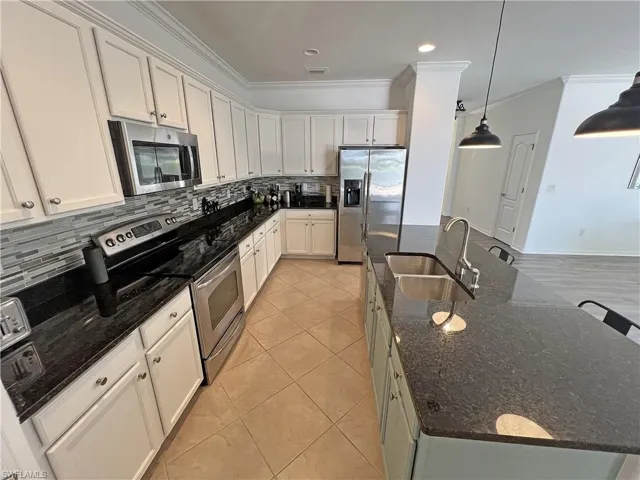 Kitchen featuring white cabinets, dark granite counters, backsplash, stainless steel appliances, and sink in kitchen island