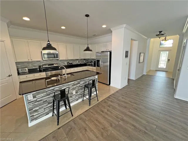 Kitchen featuring white cabinetry, hanging light fixtures, a center island with sink, light hardwood / wood-style flooring, and stainless steel appliances