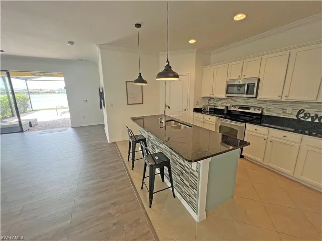 Kitchen featuring white cabinets, dark granite counters, backsplash, crown molding, stainless steel appliances, and sink in kitchen island