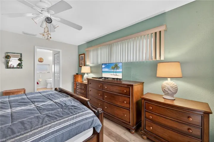 Bedroom featuring wood finished floors, a textured wall, ceiling fan, and ensuite bath