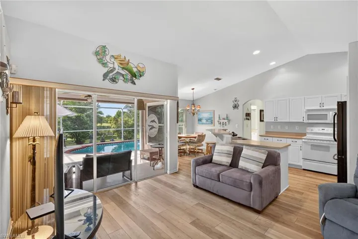 Living room with arched walkways, light wood finished floors, recessed lighting, a chandelier, and high vaulted ceiling