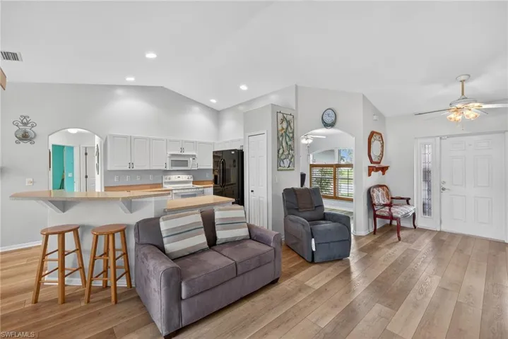 Living area with arched walkways, light wood finished floors, recessed lighting, a ceiling fan, and high vaulted ceiling