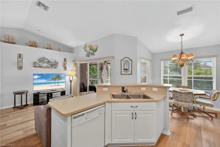 Kitchen featuring vaulted ceiling, dishwasher, light countertops, an island with sink, and light wood-type flooring