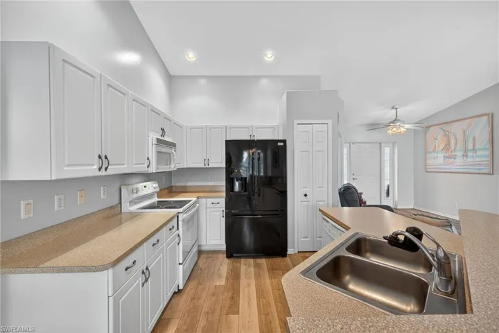 Kitchen with white appliances, light wood finished floors, white cabinetry, light countertops, and ceiling fan