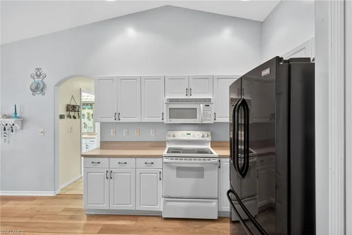 Kitchen with white appliances, light countertops, arched walkways, light wood-type flooring, and white cabinetry
