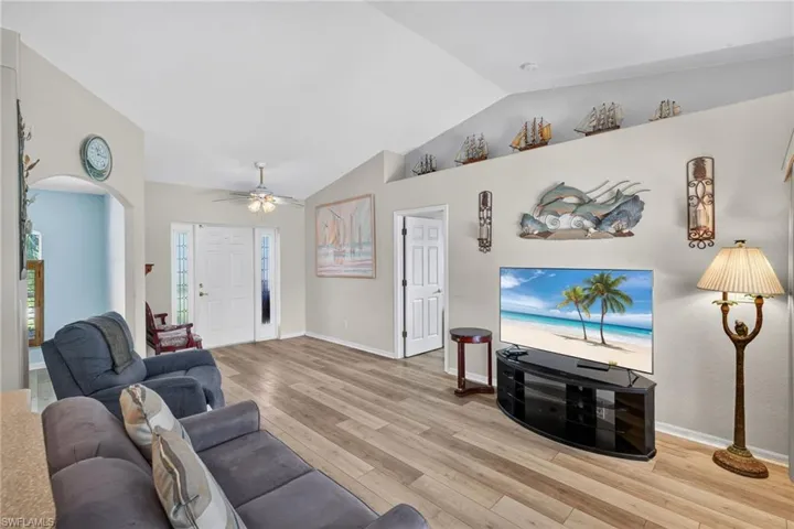 Living area with a ceiling fan, lofted ceiling, light wood finished floors, and arched walkways