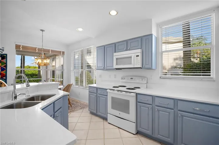Kitchen featuring white appliances, decorative light fixtures, a chandelier, light tile patterned floors, and healthy amount of natural light