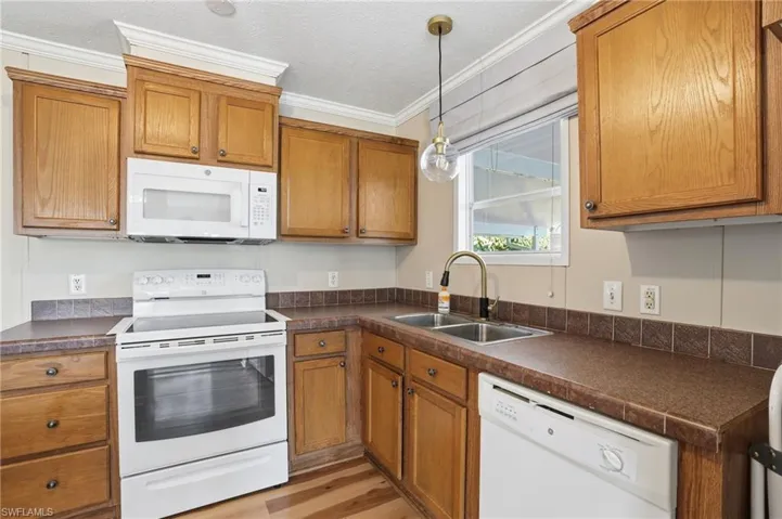Kitchen featuring white appliances, wood finish cabinetry, dark countertops, a textured ceiling, and pendant lighting