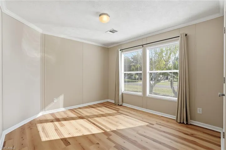 Empty room featuring light wood finished floors, crown molding, and a textured ceiling