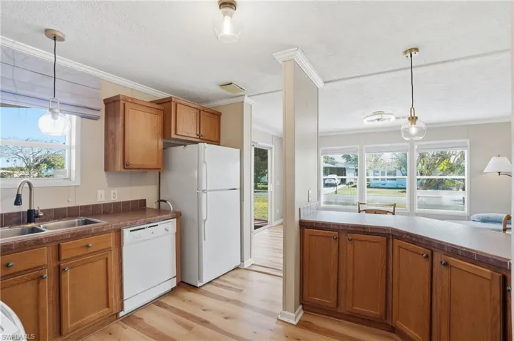 Kitchen featuring decorative light fixtures, wood finish cabinetry, white appliances, light wood-type flooring, and crown molding