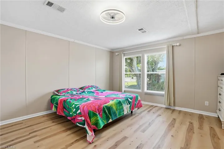 Bedroom with light wood-style flooring, a decorative wall, a textured ceiling, and crown molding