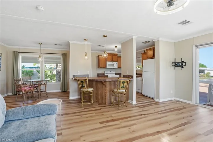 Kitchen featuring open floor plan, a kitchen bar, wood finish cabinets, white appliances, and a peninsula