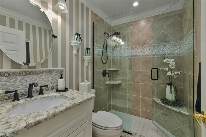 Bathroom featuring tiled shower, toilet, ornamental molding, vanity, and backsplash