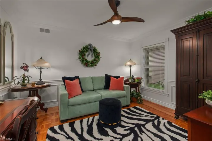 Living area with visible vents, a ceiling fan, a wainscoted wall, crown molding, and a decorative wall