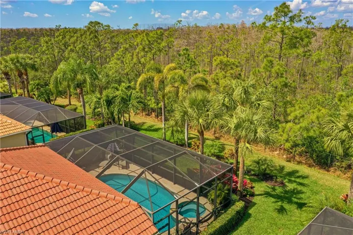 View of swimming pool featuring a pool with connected hot tub, a lawn, a patio area, glass enclosure, and a forest view