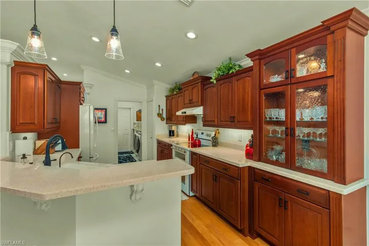 Kitchen featuring electric stove, washer / clothes dryer, a peninsula, vaulted ceiling, and under cabinet range hood