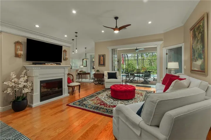 Living room with a glass covered fireplace, ceiling fan, wood finished floors, crown molding, and recessed lighting