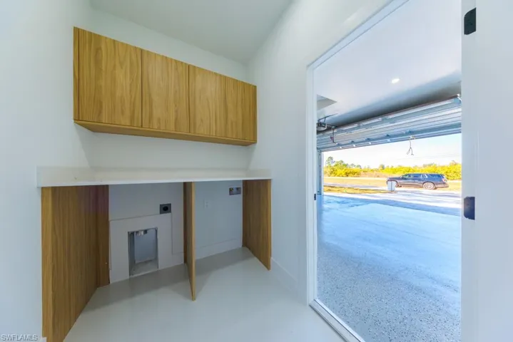 Washroom with electric dryer hookup, cabinet space, and finished concrete floors