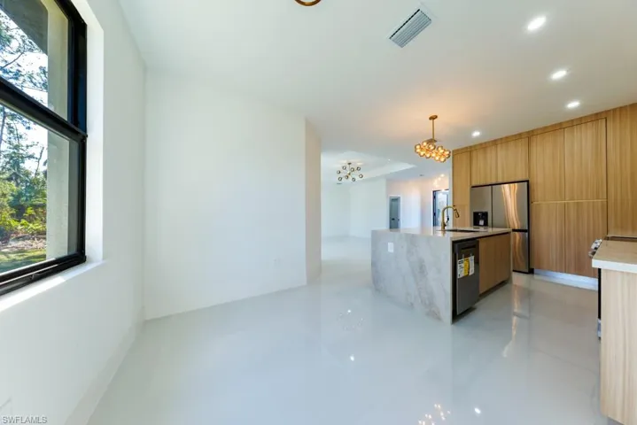Kitchen featuring light tile patterned floors, stainless steel fridge, light stone counters, hanging light fixtures, and an island with sink