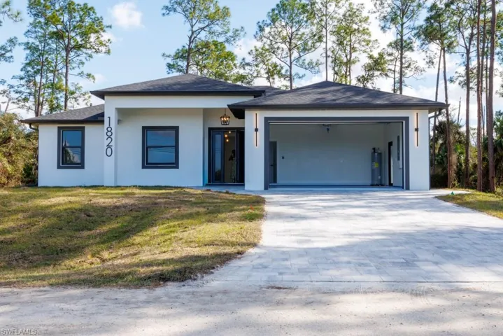 View of front of home featuring decorative driveway, a front yard, an attached garage, stucco siding, and a shingled roof