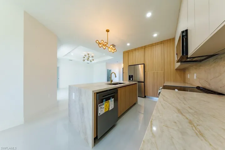 Kitchen with light stone countertops, decorative light fixtures, stainless steel appliances, modern cabinets, and a chandelier