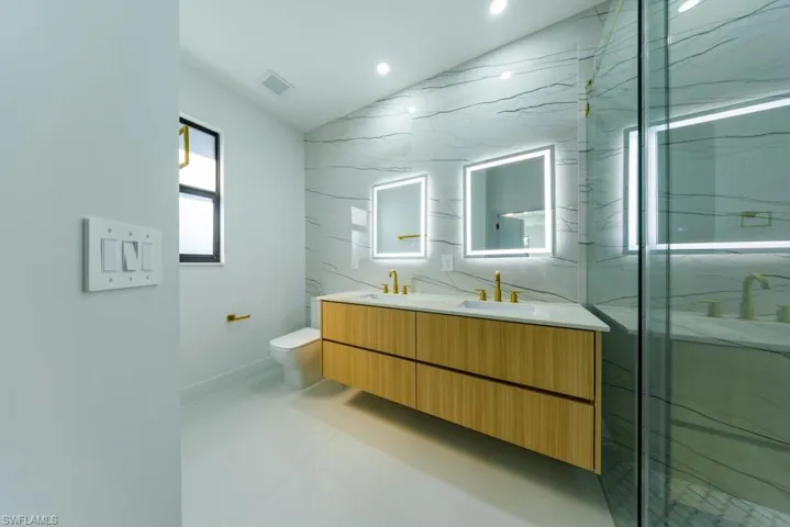 Bathroom with double vanity, tile walls, recessed lighting, vaulted ceiling, and a marble finish shower