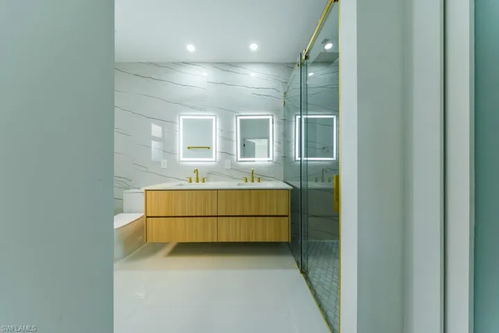 Full bath featuring double vanity, a marble finish shower, tile walls, recessed lighting, and light tile patterned floors