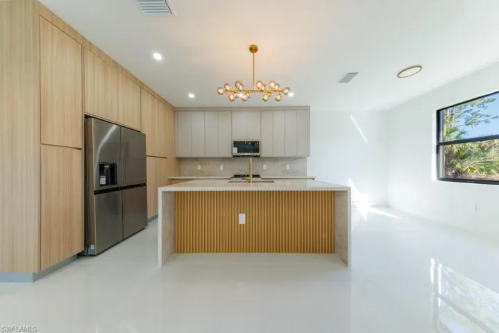 Kitchen with modern cabinets, stainless steel appliances, hanging light fixtures, light stone counters, and backsplash