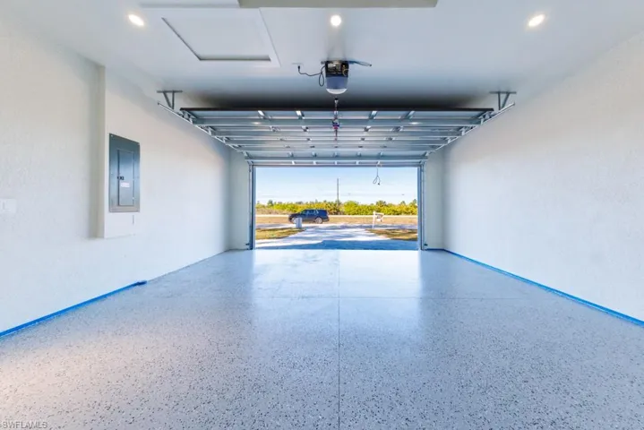 Garage with electric panel, a textured wall, recessed lighting, and a garage door opener